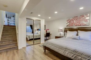 A bedroom with a large bed, a nightstand, a desk, a chair, a wardrobe, and a staircase leading to an upper level. - 2 Master Suites with King beds fast Wifi (Centennial)