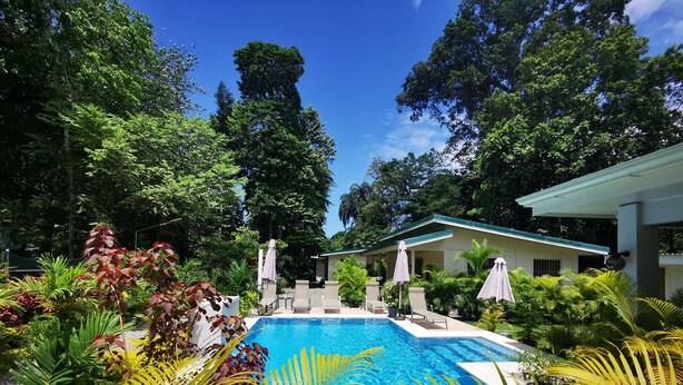 A swimming pool surrounded by lush greenery and a building with a covered patio area. - Casa mindanao apartments, AC+WIFI + swimming pool. (Limon)