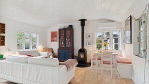 Ein gemütliches Wohnzimmer mit einem weißen Sofa, einem Holzschrank, einem Kamin und einem Essbereich mit Tisch und Stühlen.