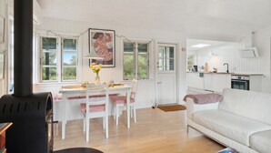 Ein gemütliches Wohnzimmer mit einem weißen Sofa, einem Esstisch mit Stühlen und einer Küchenzeile mit weißen Schränken und einem Herd.