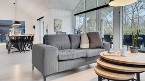 Een moderne woonkamer met een grijze bank, een ronde houten tafel en een eethoek met een witte tafel en stoelen.