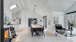 Een modern interieur met een lange eettafel, zwarte stoelen, een open haard en grote ramen met uitzicht.