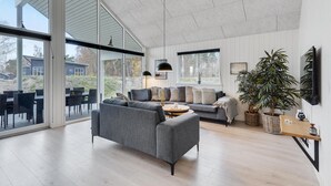 Een ruime woonkamer met een grijze bank, een salontafel en een groot raam met uitzicht op de omgeving.