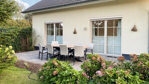 Una casa con un patio, un tavolo con sedie e un giardino fiorito.