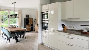 Una cucina moderna con mobili bianchi, forno a incasso e zona pranzo con tavolo e sedie in legno.