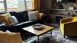 A living room with a black leather sofa, yellow armchairs, a wooden coffee table, a large flat-screen TV, and a ceiling fan. - City Overlook cabin  (Pigeon Forge)