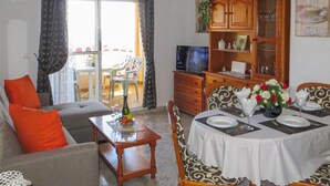 Un salon avec un canapé, une table à manger dressée pour deux personnes et un téléviseur.