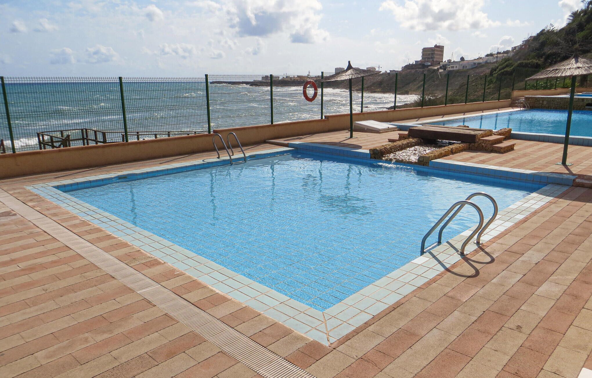 Une piscine avec vue sur la mer, une bouée de sauvetage et un chemin pavé.