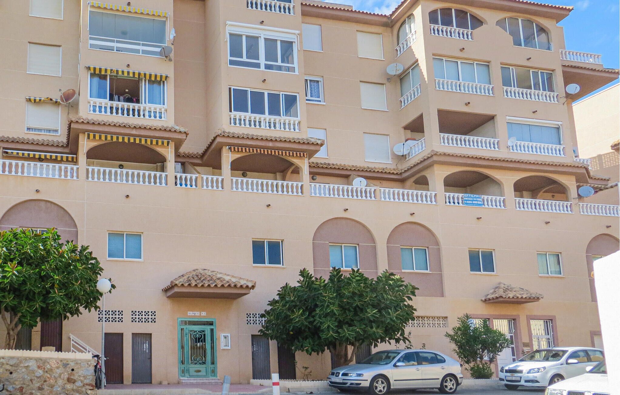 A multi-story residential building with balconies, a green door, and a car parked in front.