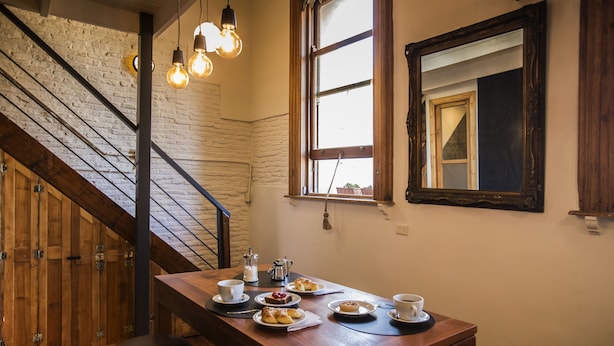 A wooden dining table with plates of food and cups, a staircase with exposed brick walls, and hanging light fixtures. - YOUR PLACE IN THE HEART OF BUENOS AIRES (CABA)
