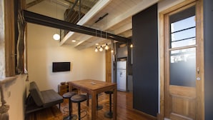 A modern kitchen with wooden flooring, a dining area with stools, a flat-screen TV, and a wooden door. - YOUR PLACE IN THE HEART OF BUENOS AIRES (CABA)