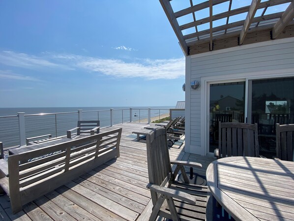 A wooden deck with outdoor seating, overlooking a beach. - Stunning, light-filled beachfront sanctuary with full views of Delaware Bay. (Prime Hook Beach)