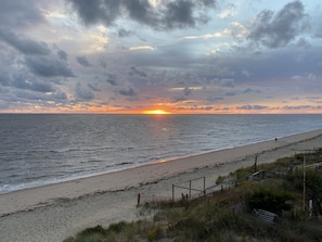 Una spiaggia al tramonto, con onde e una recinzione in primo piano.