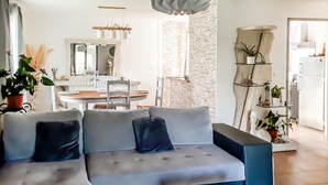 Ein Wohnzimmer mit einer Couch, einem Esstisch mit Stühlen und einer Küchenzeile mit Kühlschrank und einer Pflanze.