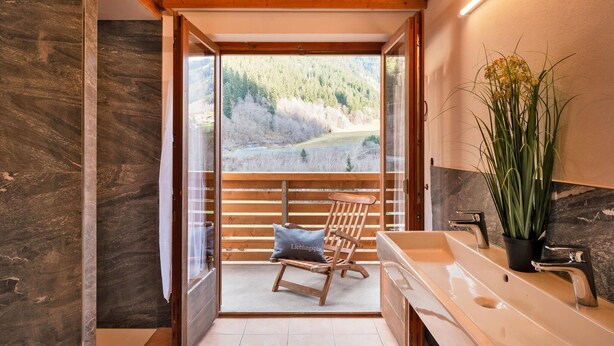 Un baño con un banco de madera, un lavamanos y vistas a un área boscosa.