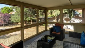 Une véranda avec de grandes fenêtres, des meubles en osier et une vue sur le jardin.
