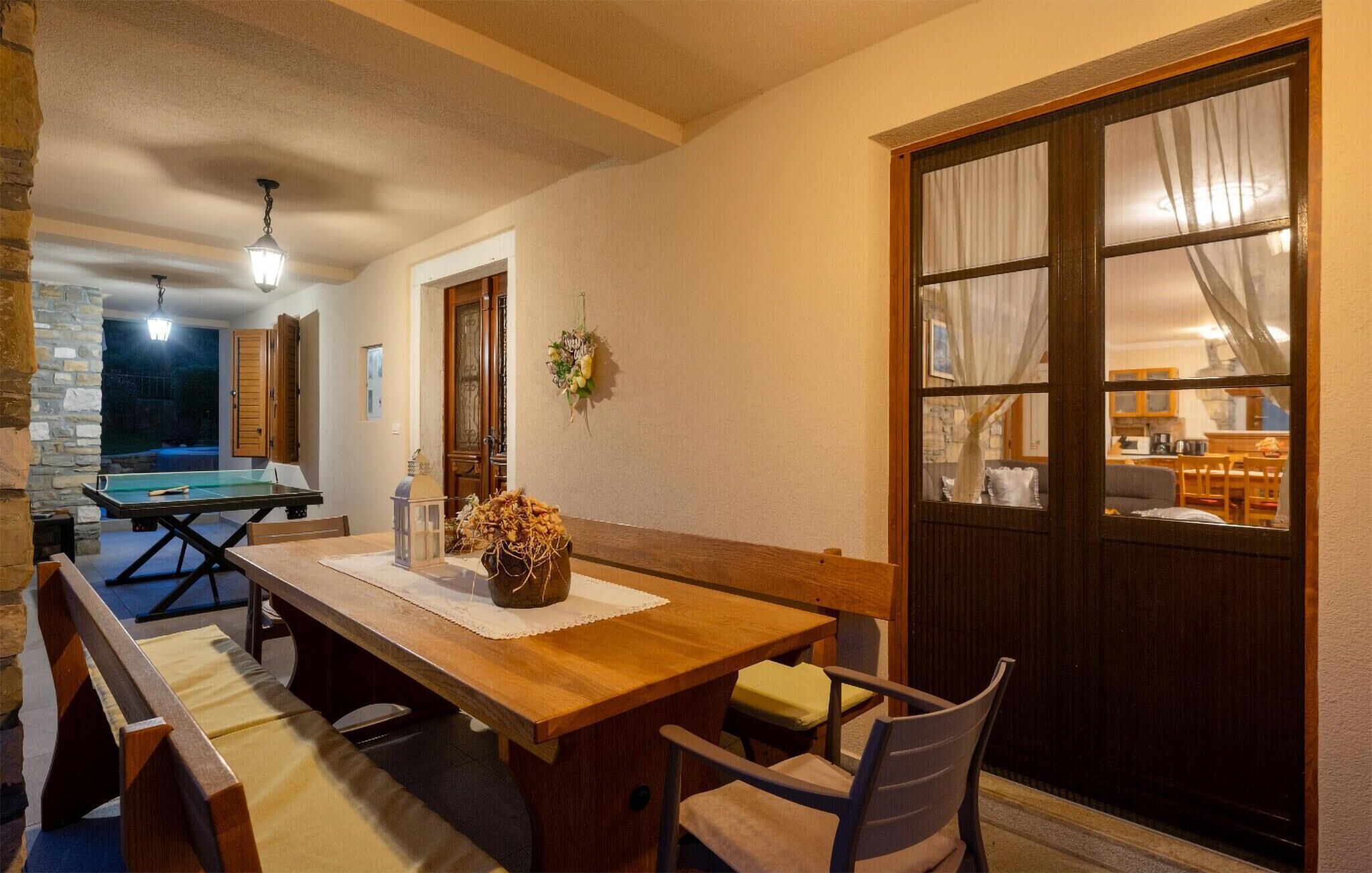 Un coin repas chaleureux avec une table et des bancs en bois, un vase décoratif et une vue sur la cuisine grâce à une grande fenêtre.