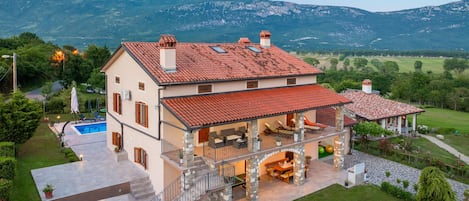 A two-story house with a swimming pool, stone staircase, and a view of mountains.