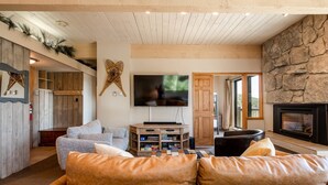 A cozy living room with a stone fireplace, a flat-screen TV mounted on the wall, and a wooden entertainment unit.