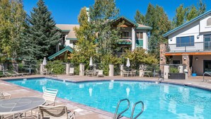 A swimming pool with lounge chairs and umbrellas, surrounded by trees and buildings.
