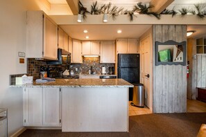A kitchen with a central island, wooden cabinets, a black refrigerator, and a tiled backsplash. - Hike-In/Hike-Out w/Amazing Panoramic Views + Heated Pool-Hot Tub-Gym Access-Fireplace-Elevator-Deck (Steamboat Springs)