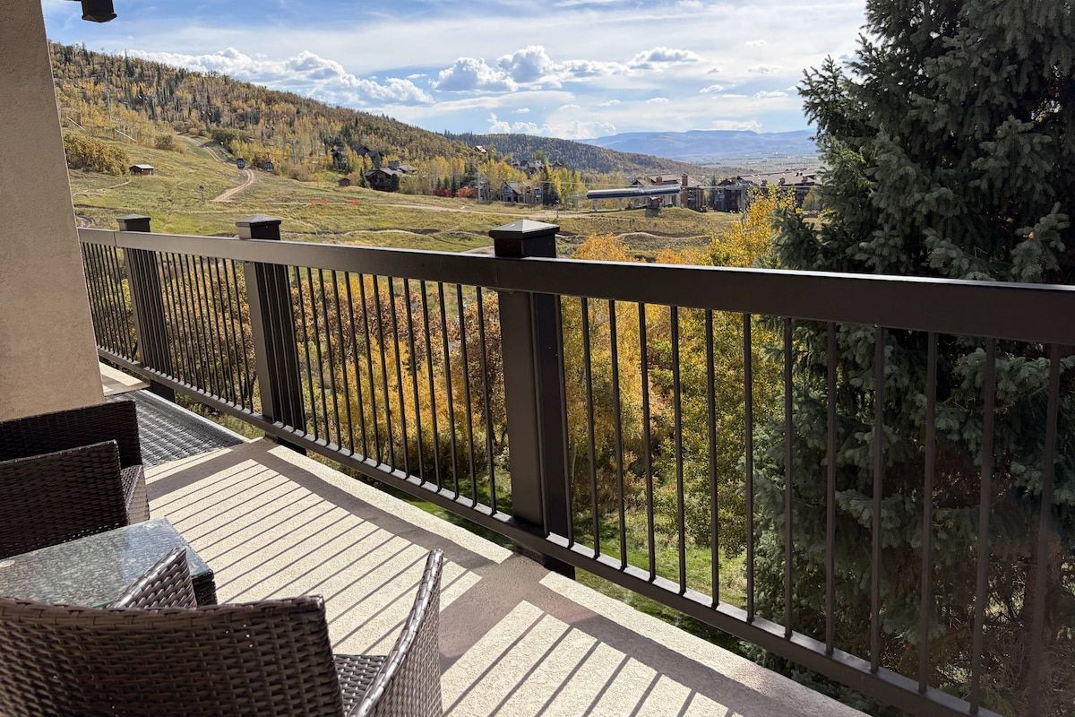 A balcony with wicker furniture and a view of a hilly landscape.