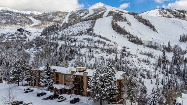 A snow-covered mountain resort with a building featuring multiple floors and a parking area.