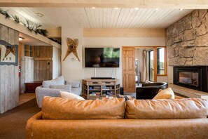 A cozy living room with a stone wall, a fireplace, a flat-screen TV, and a comfortable seating area. - Ski In/Out w/Amazing Scenic Views+Pool-HotTub-Gym (Steamboat Springs)