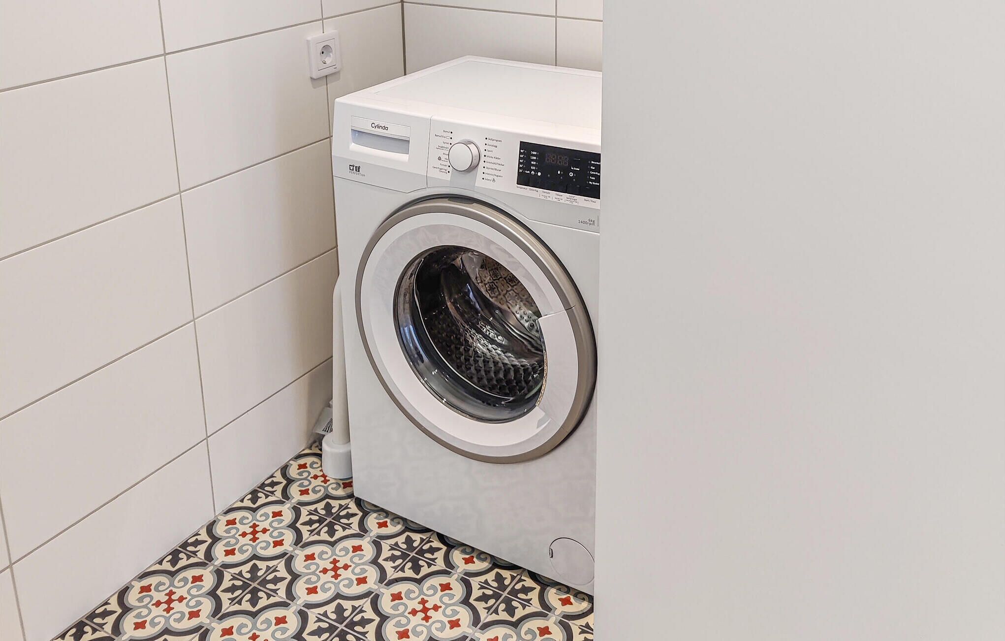 Een voorlader wasmachine in een kleine wasruimte met betegelde muren en een vloer met patroon.