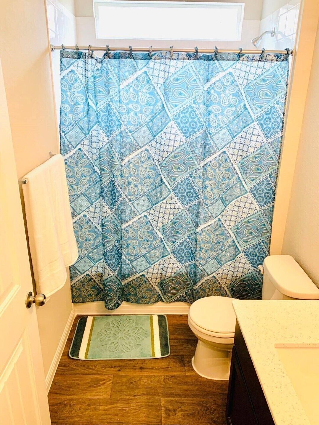 Une salle de bain avec un rideau de douche à motifs, des toilettes et un petit tapis sur le sol.