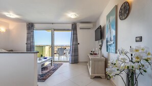 Een hotelkamer met balkon, een zithoek en een woonruimte met televisie en kunstwerk.