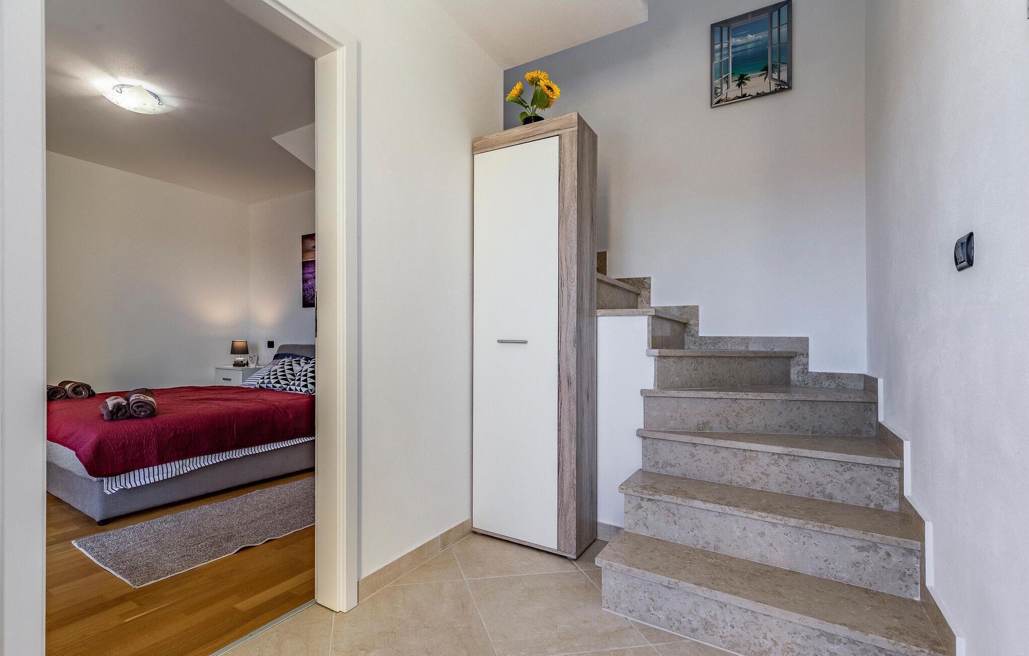 Ein Schlafzimmer mit einem Bett, einem Nachttisch, einer roten Decke und einem Bild an der Wand.