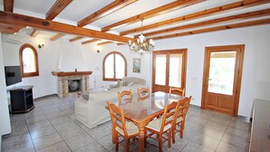 Un amplio salón con techo de madera, chimenea, mesa de comedor con sillas y televisor.