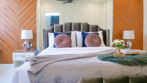 A bedroom with a large bed, a wooden herringbone wall pattern, a ceiling fan, and a nightstand with a lamp and a book. - Exquisite Pool Villa I (Pattaya)