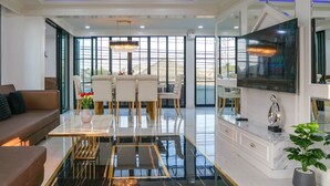 A modern living room with a dining area, large windows, a chandelier, and a TV. - Exquisite Pool Villa I (Pattaya)