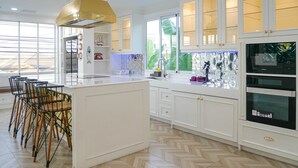 A modern kitchen with white cabinetry, a central island, and a dining area with chairs. - Exquisite Pool Villa I (Pattaya)