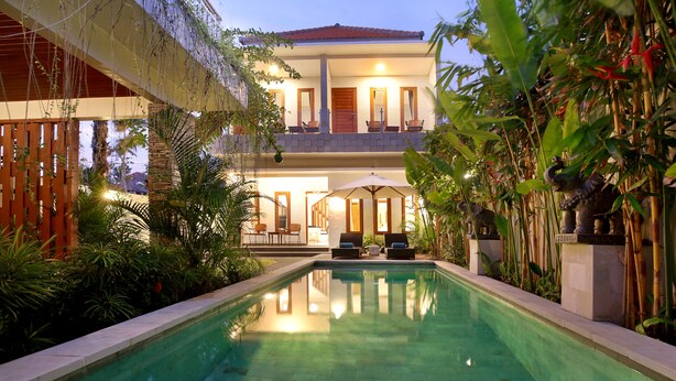 A pool area with a two-story building, outdoor seating, and lush greenery. - Askara Villa Uluwatu (Ungasan)