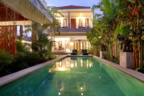 A pool area with a two-story building, outdoor seating, and lush greenery.