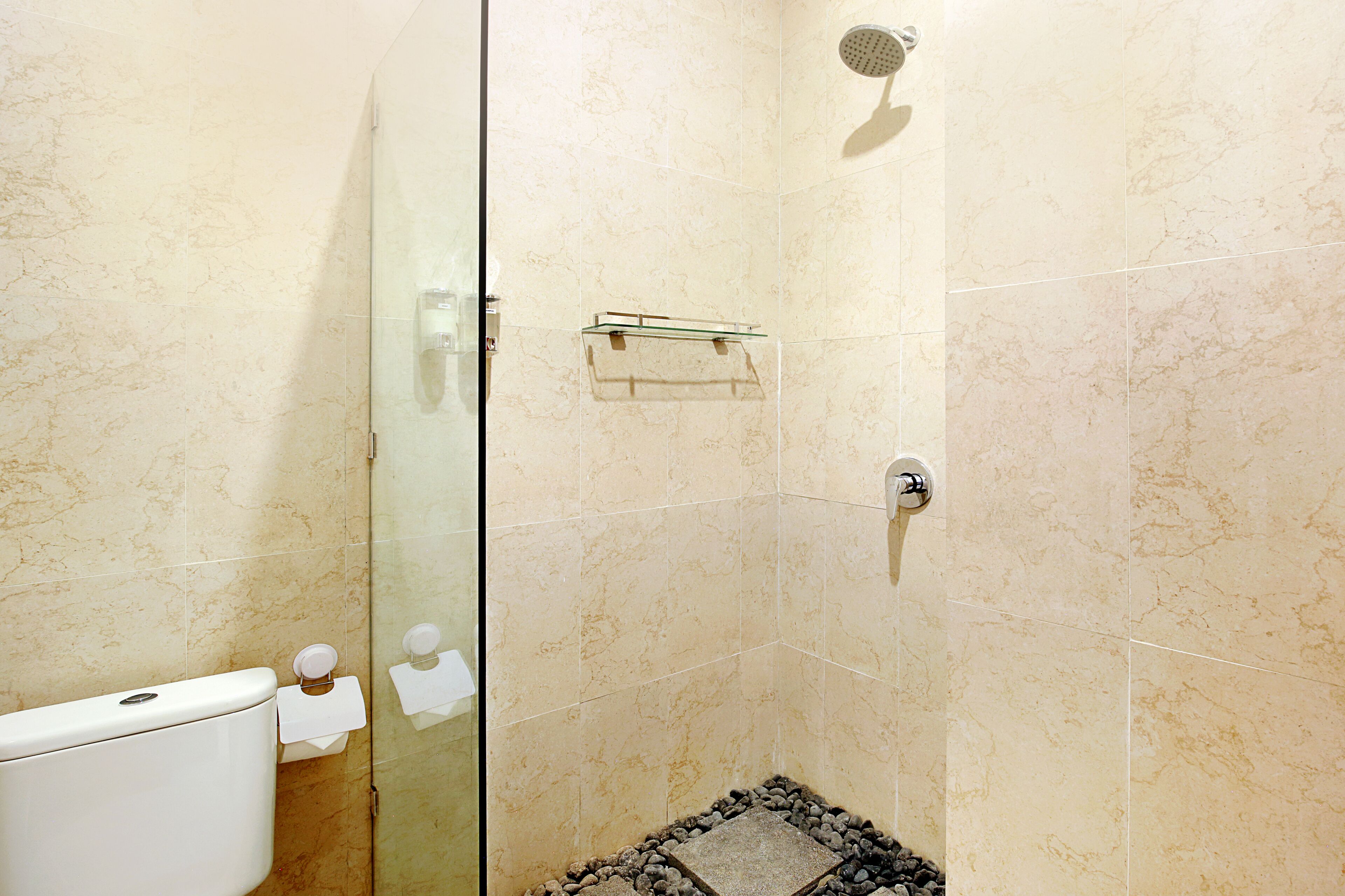 Een badkamer met een douchecabine van glas, een toilet en een klein plankje met toiletartikelen.