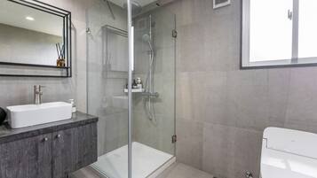 A modern bathroom with a glass-enclosed shower, a white sink, and a toilet.