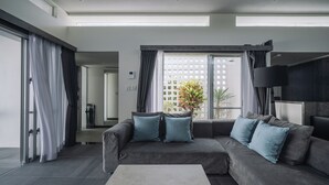 A modern living room with a grey sectional sofa, a flat-screen TV, and a large window with a view of greenery.
