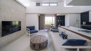 A modern living room with a flat-screen TV, a wooden coffee table, a sofa with blue cushions, and a dining area with chairs and a table.