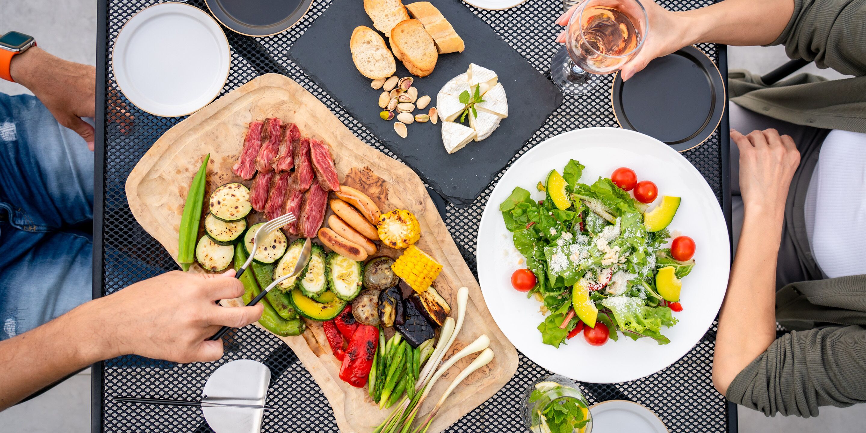 Une table garnie d’une variété de plats, notamment des légumes grillés, de la viande et une salade, ce qui laisse supposer qu’il s’agit d’un repas partagé.