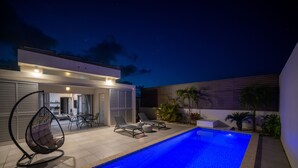 A modern outdoor pool area with a clear blue pool, lounge chairs, and a hanging chair.