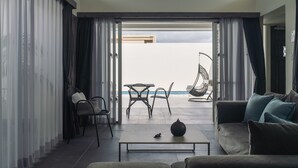 A modern living room with a sofa, coffee table, and chairs. A balcony with a table and chairs is visible through the open door.