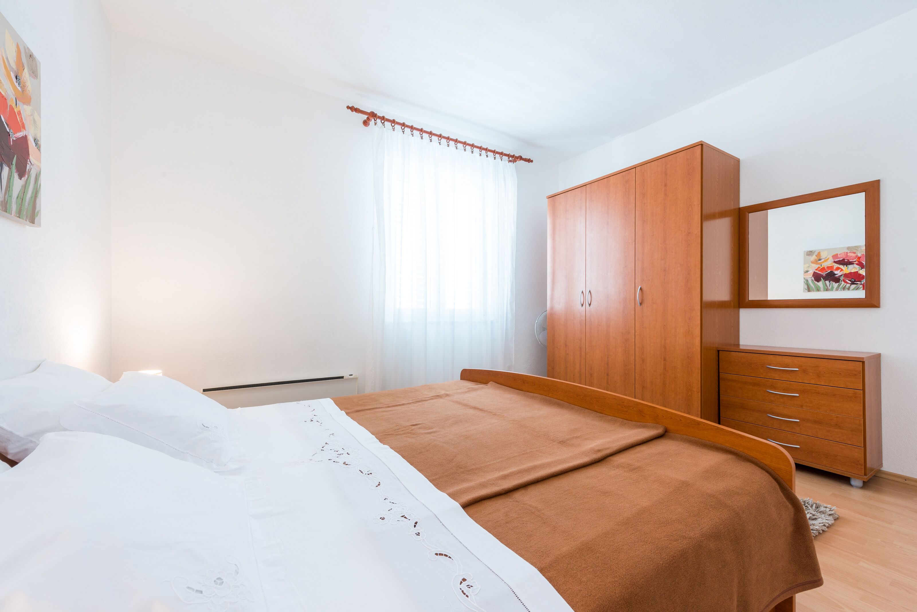Ein Schlafzimmer mit einem Bett, einem Holzschrank, einem Schminktisch, einem Spiegel und einem Fenster mit Vorhängen.