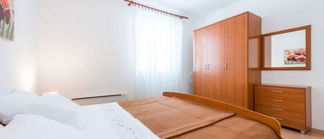 Ein Schlafzimmer mit einem Bett, einem Holzschrank, einem Schminktisch, einem Spiegel und einem Fenster mit Vorhängen.