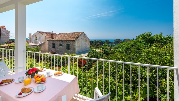 A balcony with a table set for breakfast, overlooking a lush garden and a clear blue sky.