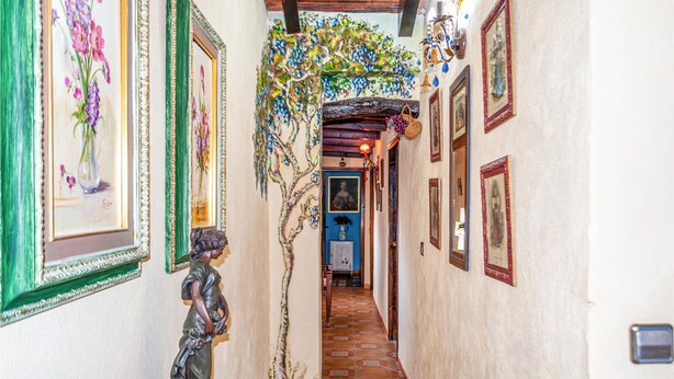 A narrow hallway with framed artwork on the walls, a statue, and a tiled floor. - Lovely home in Arenas del Rey with WiFi (Arenas del Rey)