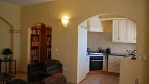 A compact living space with a kitchen, a seating area with a bookshelf, and a dining table. - Casa Biontica (Cómpeta)